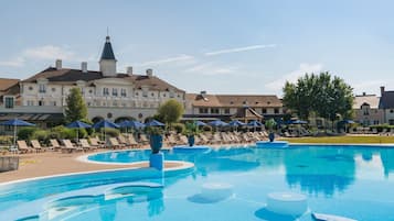 Una piscina con sillas de descanso y sombrillas, rodeada de edificios que incluyen una torre destacada.