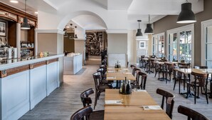 A spacious dining area with high ceilings, a long wooden table, and multiple chairs. There is a bar area with shelves of bottles and glasses.