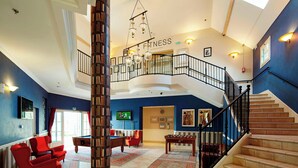 A spacious lobby with a pool table, red armchairs, a foosball table, and a staircase leading to an upper level.