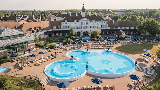 A resort with a large swimming pool, sun loungers, and a central building with a tower.