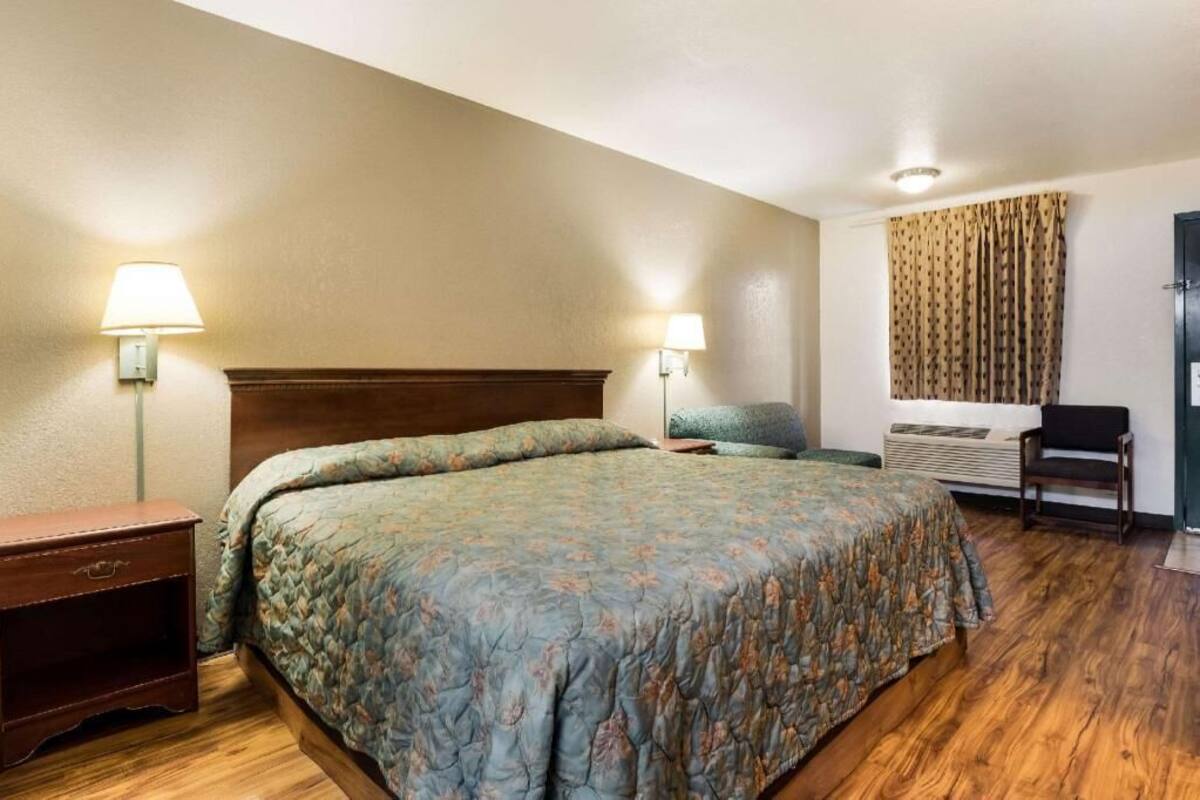 A hotel room with a bed, bedside lamps, a chair, a heater, and a door.