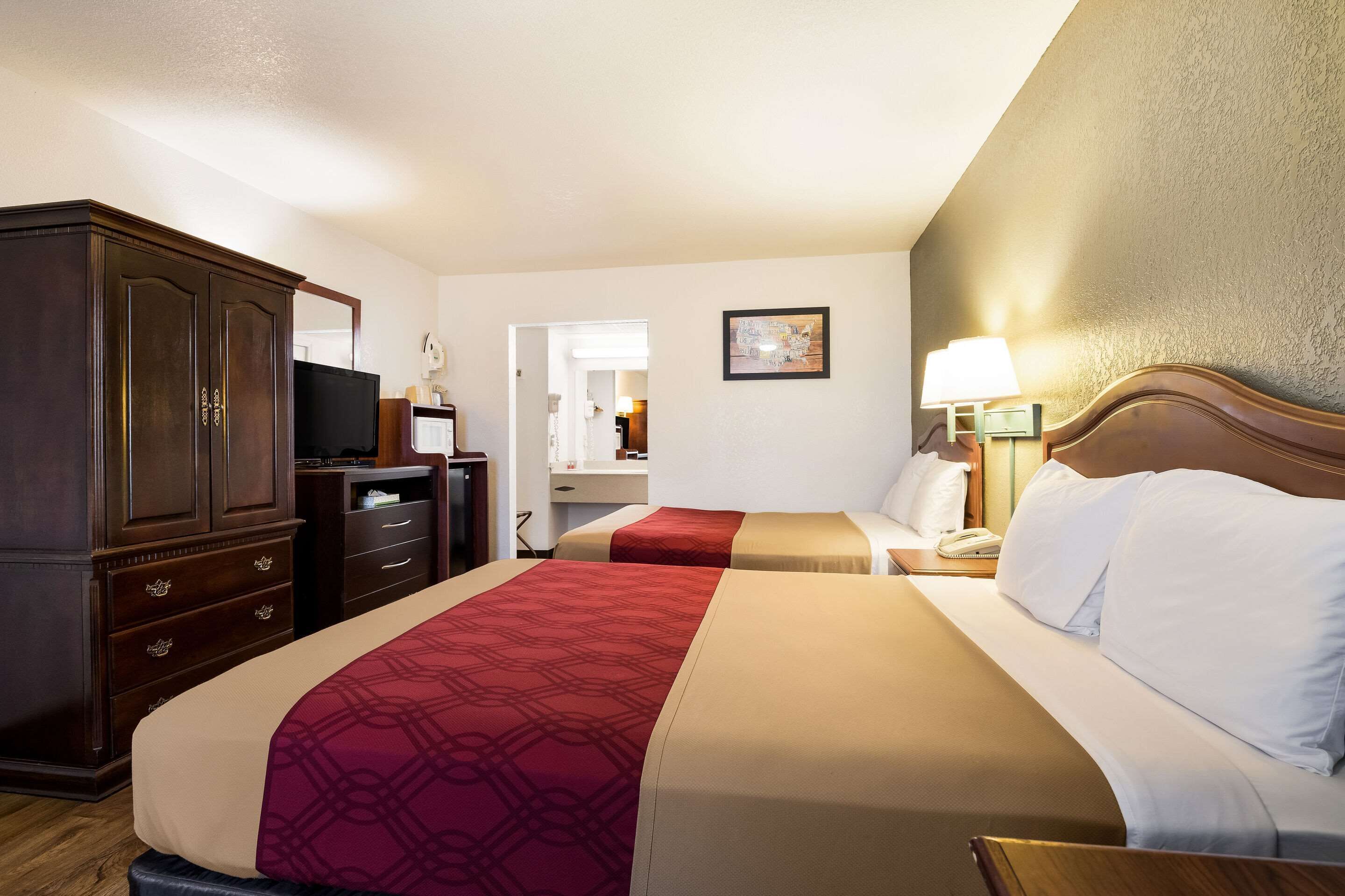 A hotel room with two beds, a wardrobe, a television, a desk, and a mirror.