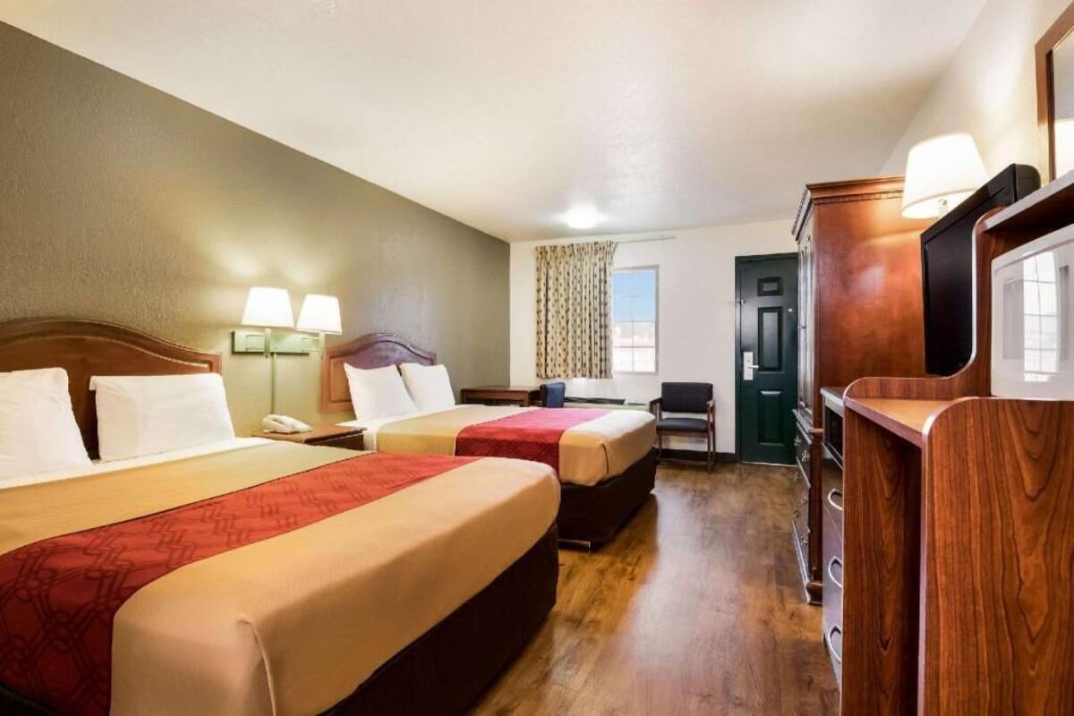 A hotel room with two beds, a desk, a chair, a dresser, and a window with curtains.