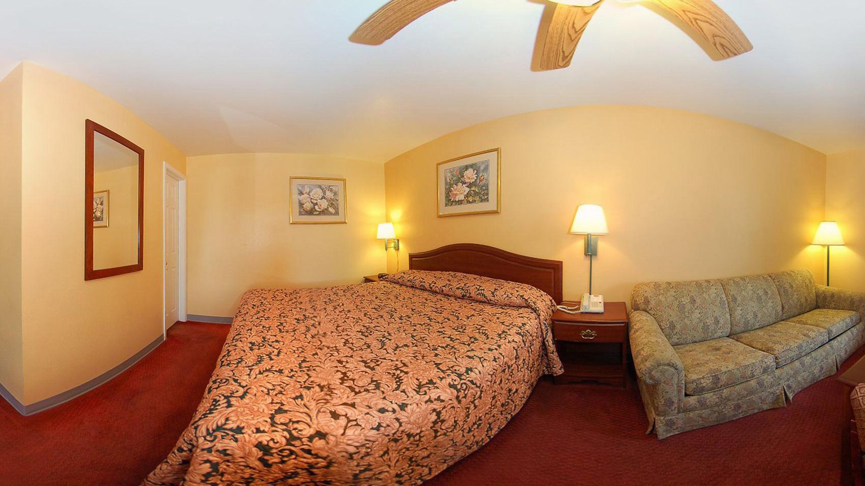 A hotel room with a large bed, a sofa, two wall-mounted lamps, and a ceiling fan.