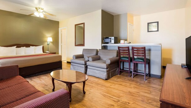 A hotel room with a bed, a sofa, a dining table, and a TV.