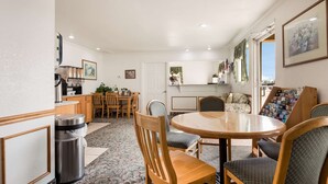 A dining area with a round table, wooden chairs, a trash can, and a kitchen in the background.