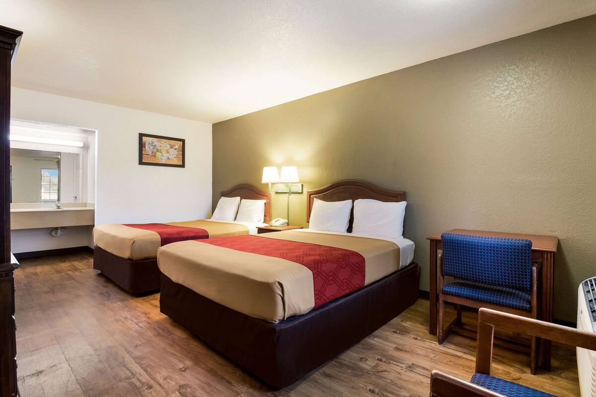 A hotel room with two beds, a chair, a desk, and a lamp.
