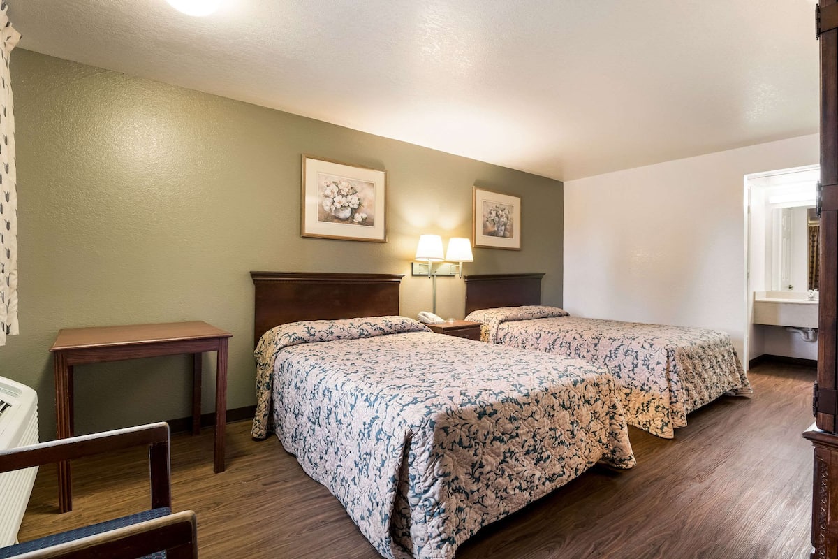 A hotel room with two beds, a wooden nightstand, a small table, and a chair.
