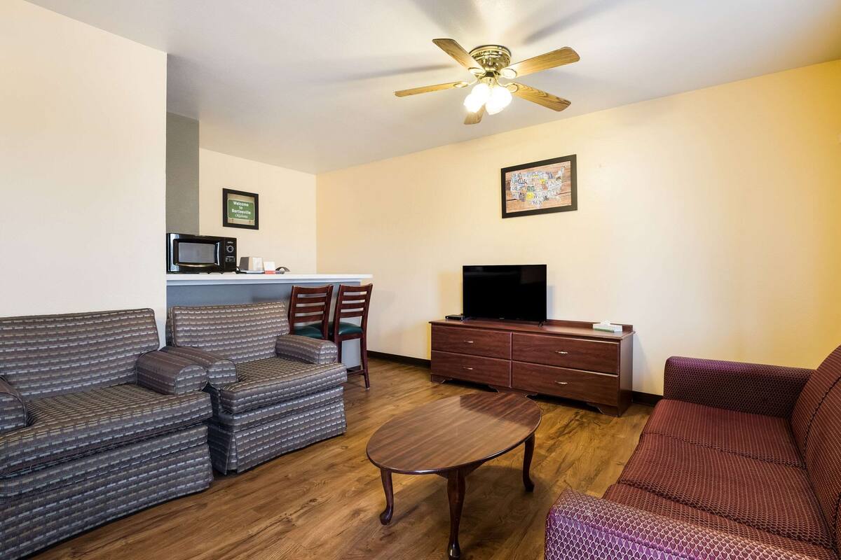 A living room with a sofa set, a wooden coffee table, a television, and a ceiling fan.