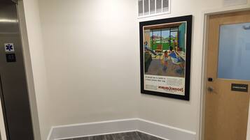 A hallway with a framed advertisement for Howard Johnson's Motor Lodge, a door labeled "Fitness Room," and an elevator with emergency exit signs.