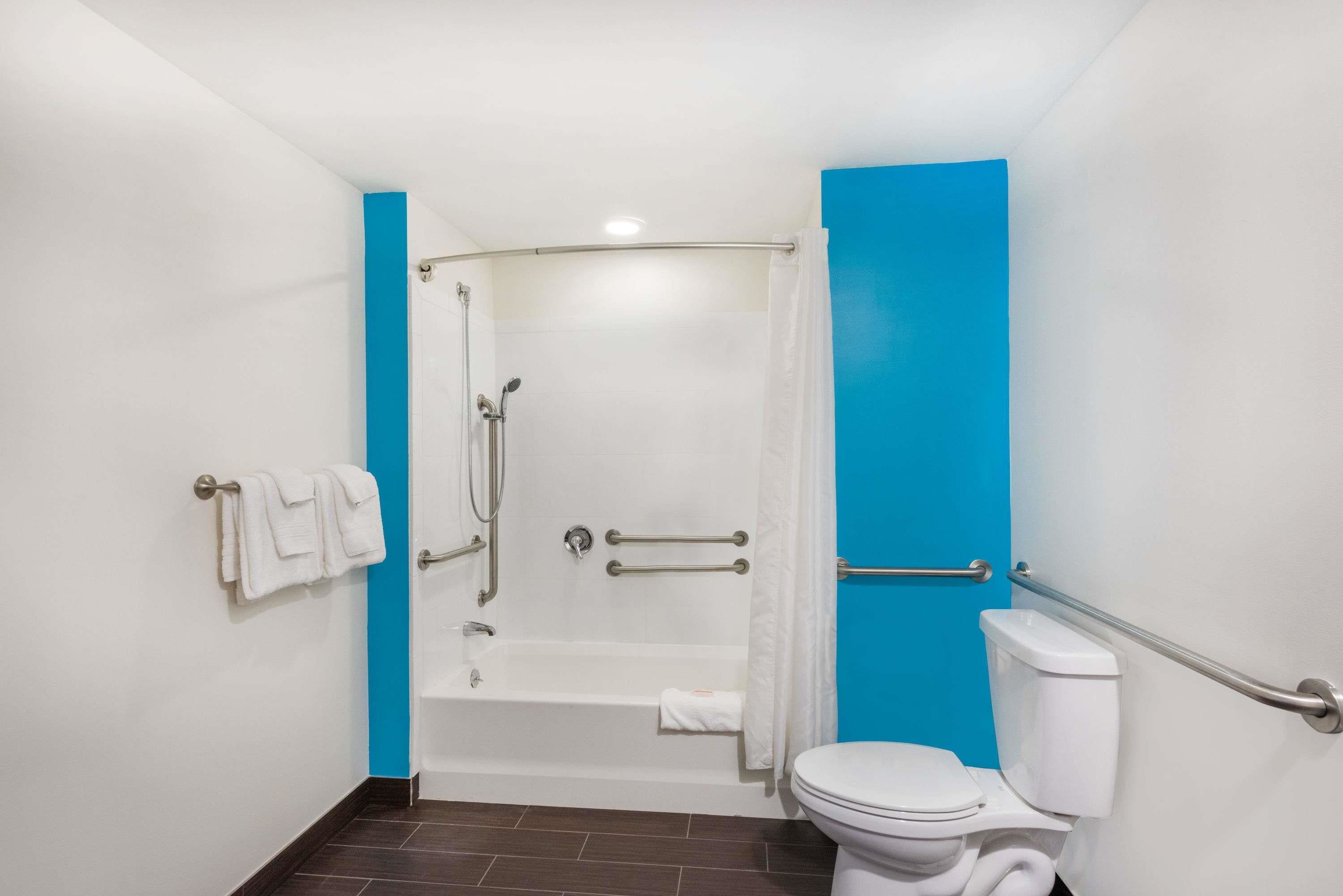 A bathroom with a bathtub, toilet, and handrails.