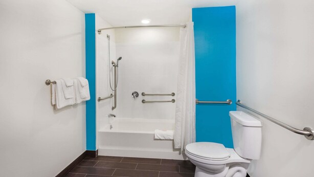 A bathroom with a bathtub, toilet, and handrails. - Howard Johnson by Wyndham Quincy/Boston (Quincy)