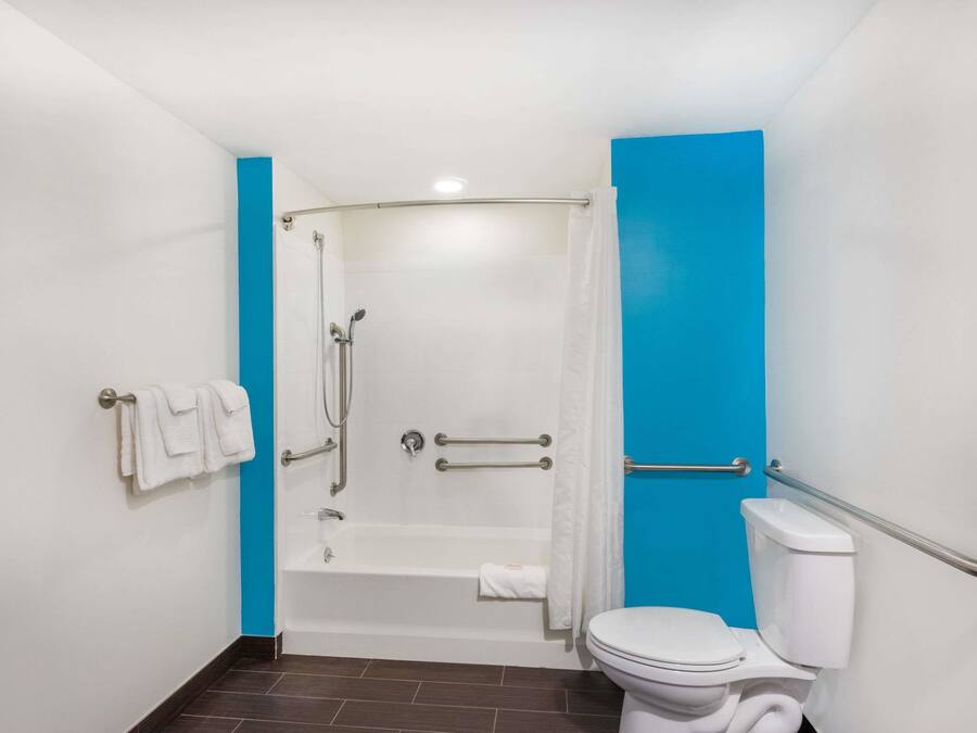 A bathroom with a bathtub, toilet, and handrails.