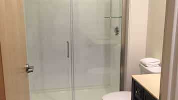 A bathroom with a glass-enclosed shower, a white toilet, and a dark tiled floor.