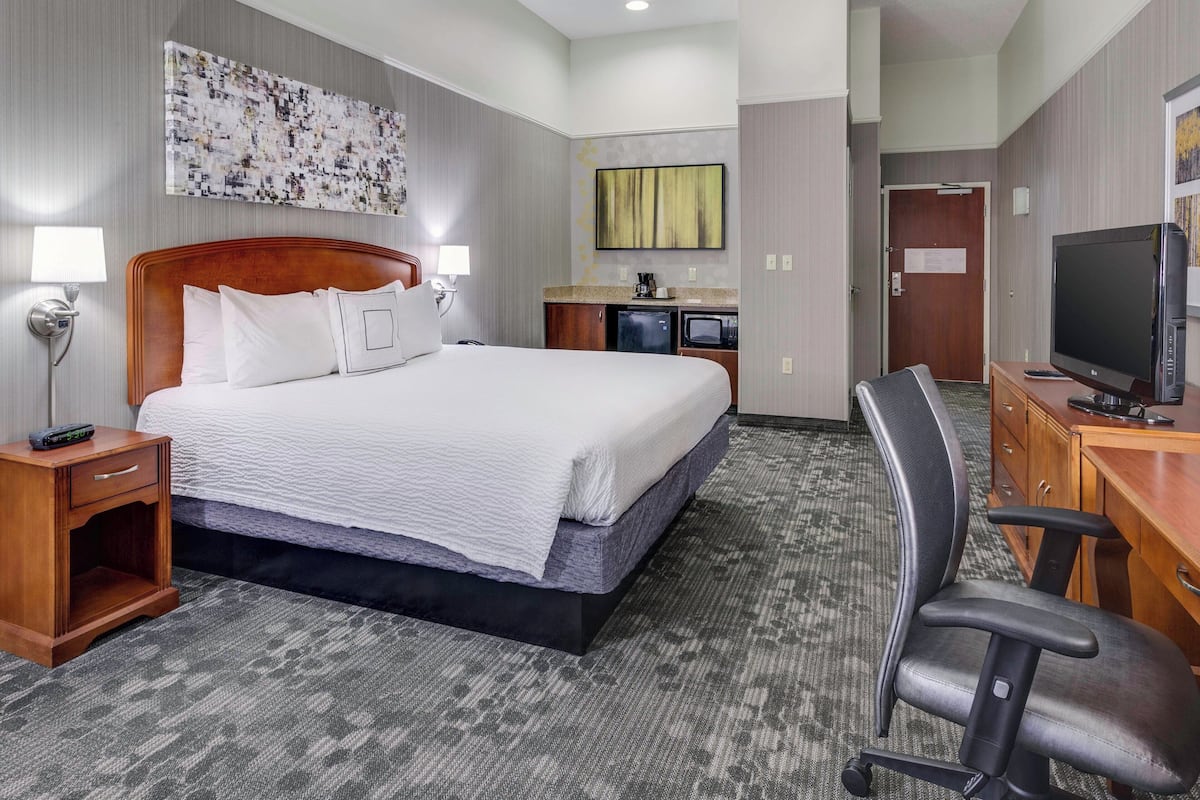 A hotel room with a large bed, a desk with a computer, a TV, a desk lamp, a small refrigerator, and a microwave.