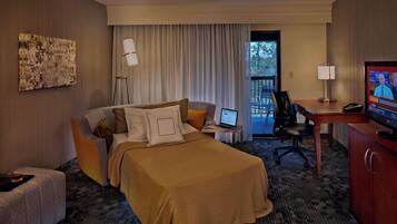 Una habitación de hotel con una cama, un escritorio con una computadora portátil, una televisión y un balcón con sillas.