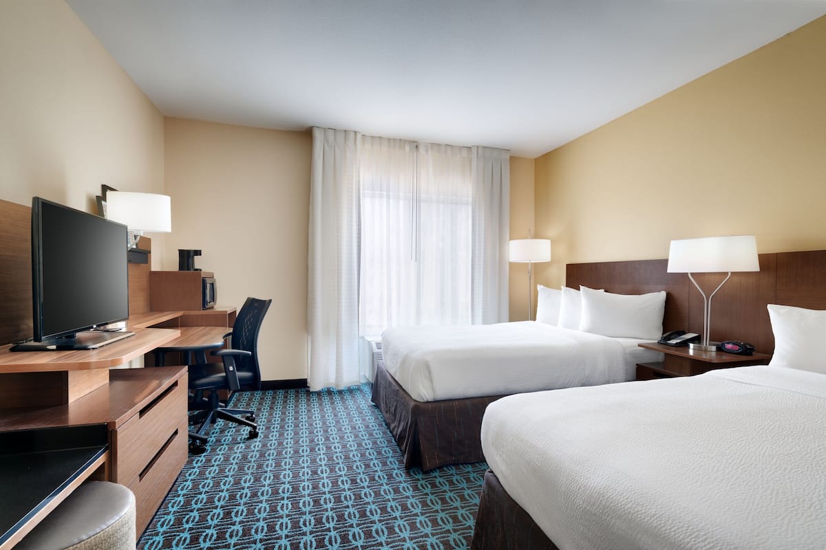A hotel room with a desk, two beds, a TV, and a window with curtains.