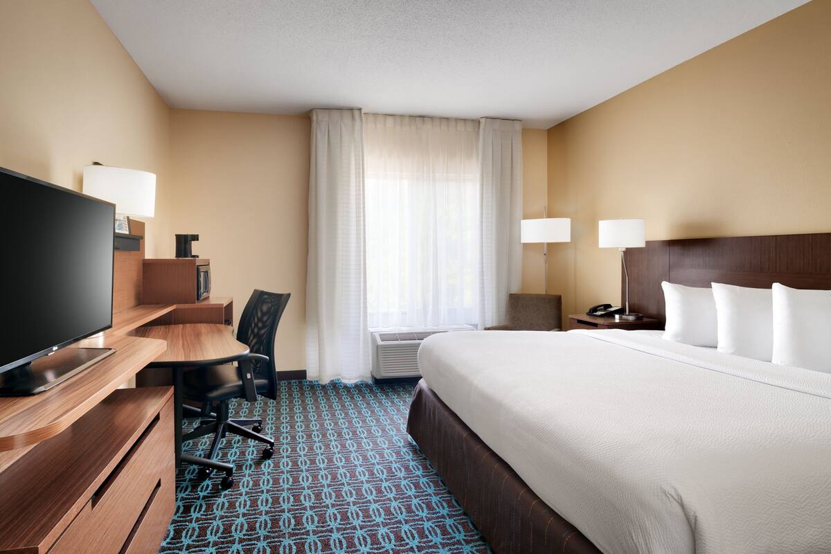 A hotel room with a bed, a desk, a television, and a chair.