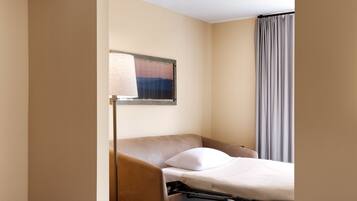 Una habitación de hotel con una cama individual, una mesita de noche, una lámpara y una ventana con cortinas.