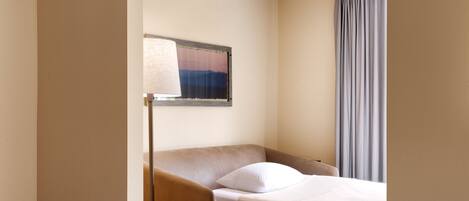 A hotel room with a single bed, a bedside table, a lamp, and a window with curtains.
