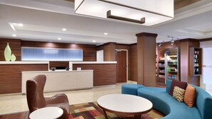 A modern hotel lobby with a reception desk, seating area, and a refrigerator stocked with beverages. - Fairfield Inn by Marriott Lexington Park Patuxent River Naval Air Station (Lexington Park)