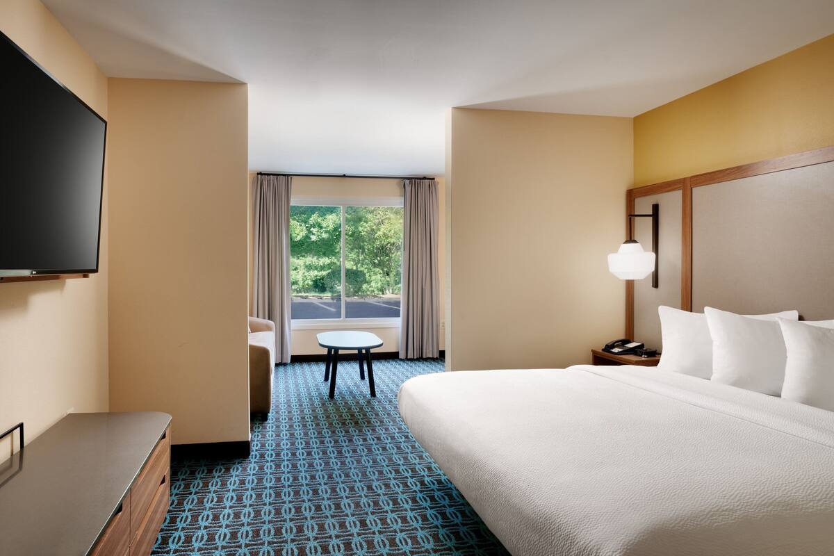 A hotel room with a large bed, a television, a desk, and a window with curtains.