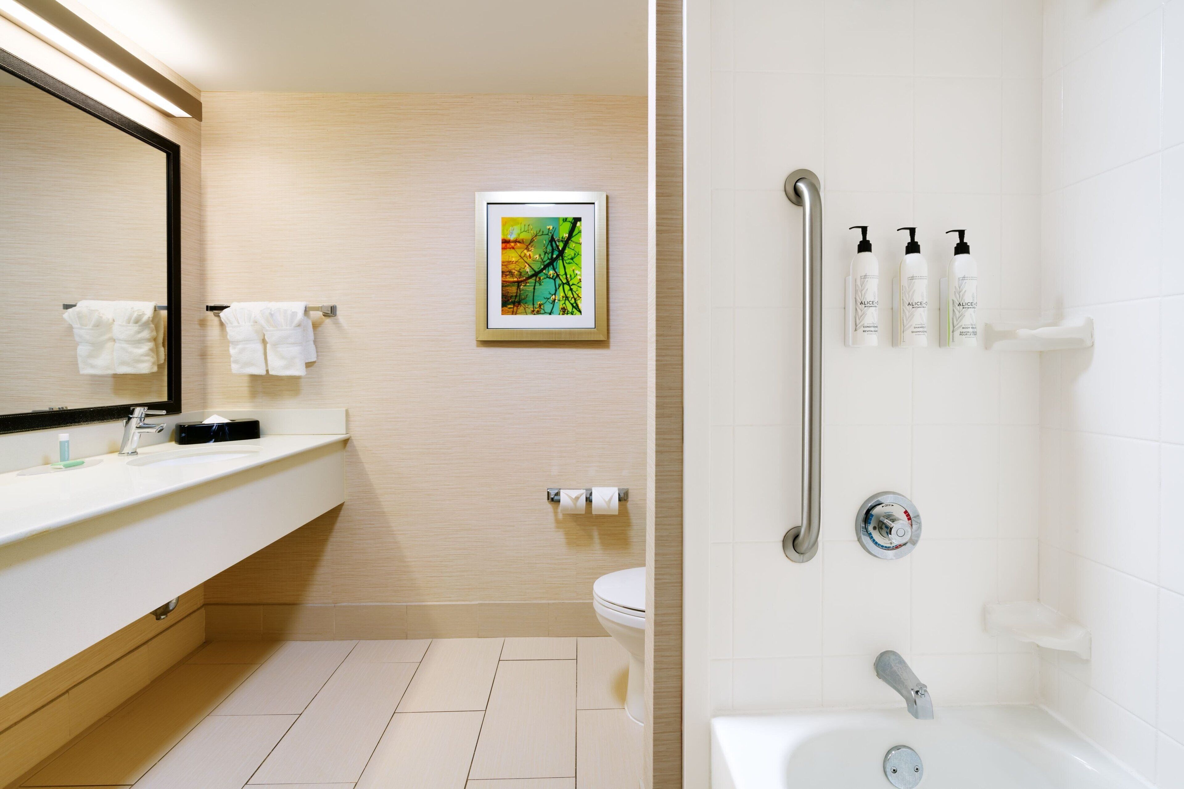 Uma casa de banho moderna com lavatório, sanita e zona de duche. Há artigos de higiene pessoal na parede e um quadro emoldurado sobre a sanita.
