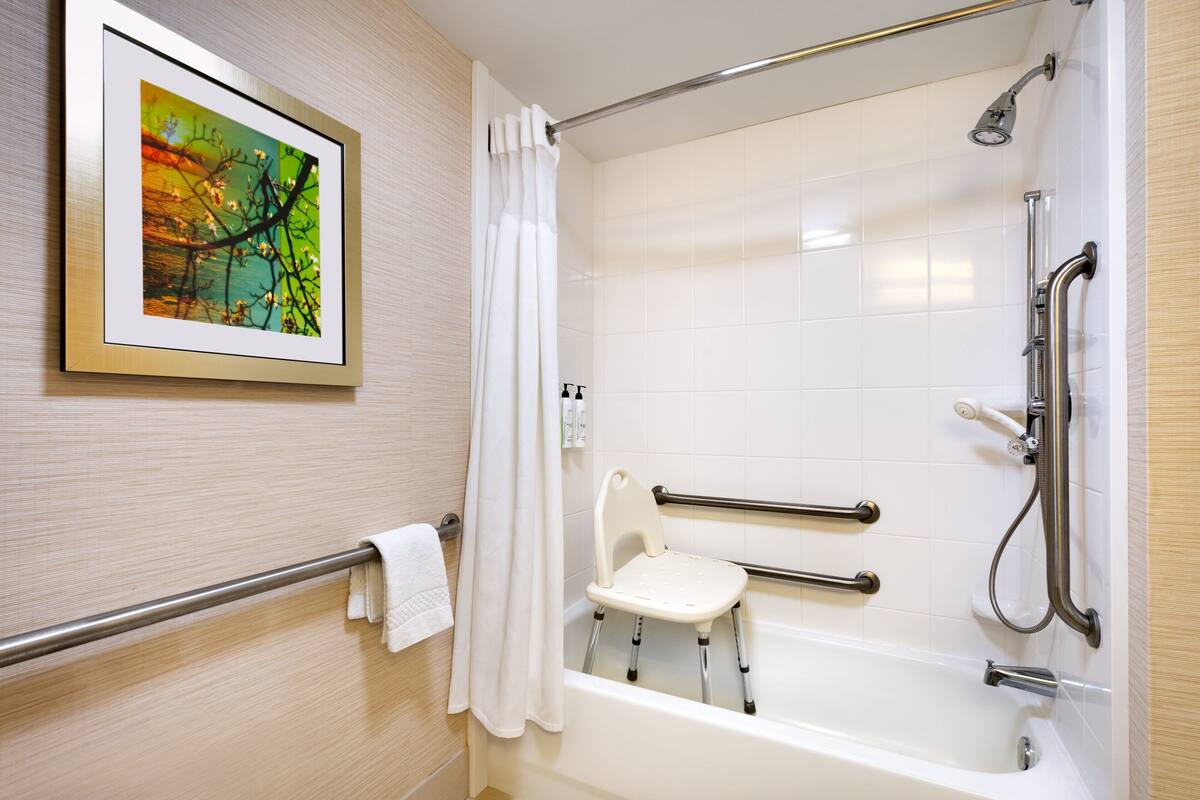 A bathroom with a bathtub, a shower, a handrail, a grab bar, and a towel rack.