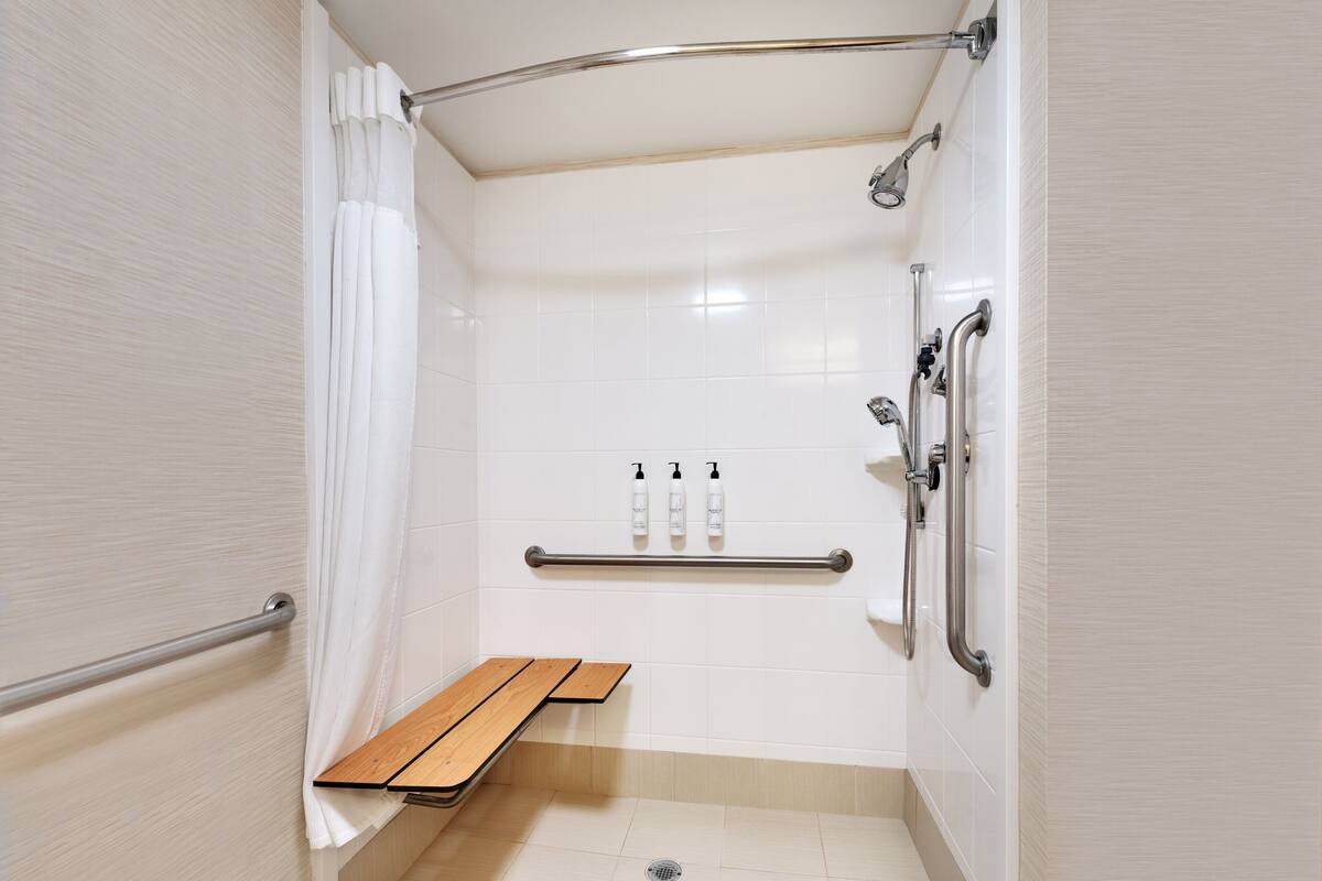 A modern shower area with a bench, grab bars, and hand sanitizer dispensers.