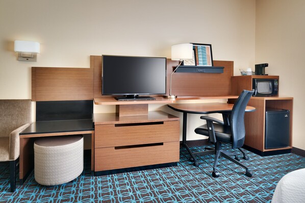 Habitación de hotel con escritorio de madera, televisor de pantalla plana, refrigerador pequeño, microondas, silla y mesita de noche.