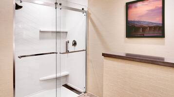 Un baño moderno con cabina de ducha de vidrio, tocador de madera y un cuadro en la pared.
