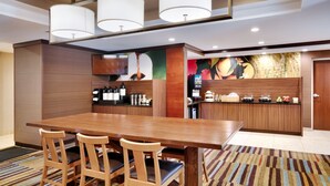 A modern dining area with a wooden table and chairs, a kitchen counter with various appliances, and a colorful mural on the wall. - Fairfield Inn by Marriott Lexington Park Patuxent River Naval Air Station (Lexington Park)