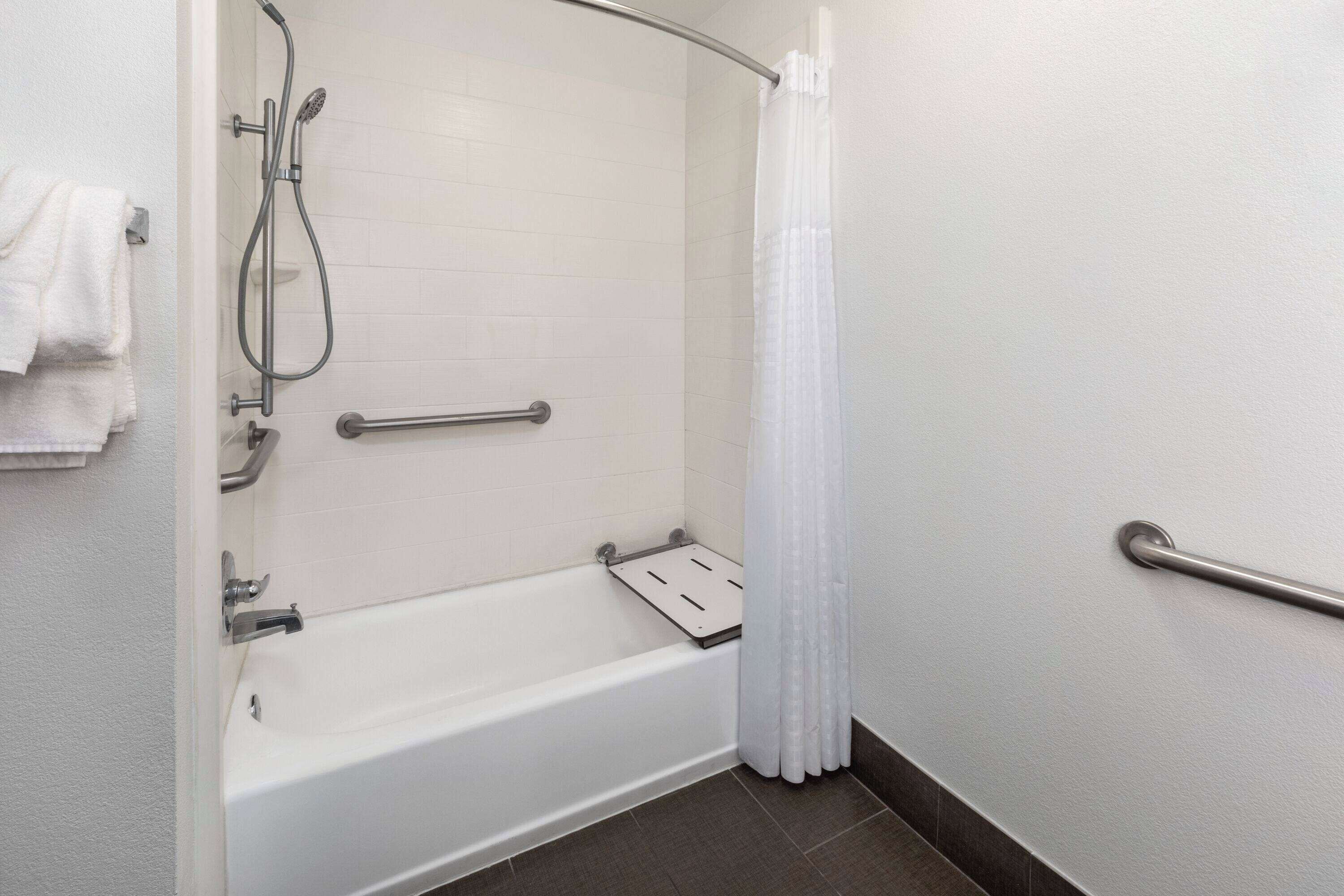 A modern bathroom with a bathtub, shower, and grab bars.
