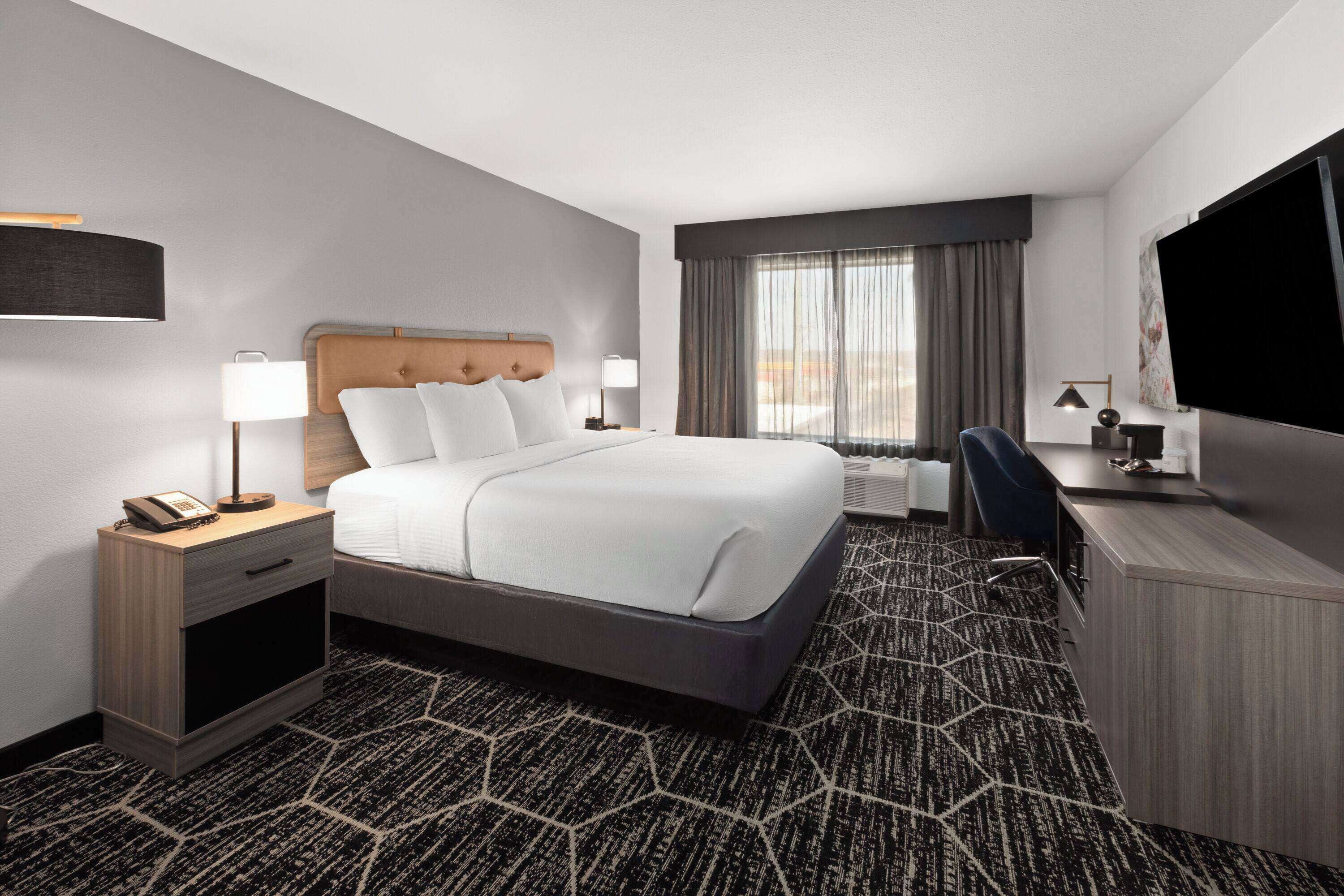 Une chambre d’hôtel avec un grand lit, un bureau avec un ordinateur, un téléviseur à écran plat et une fenêtre avec des rideaux.