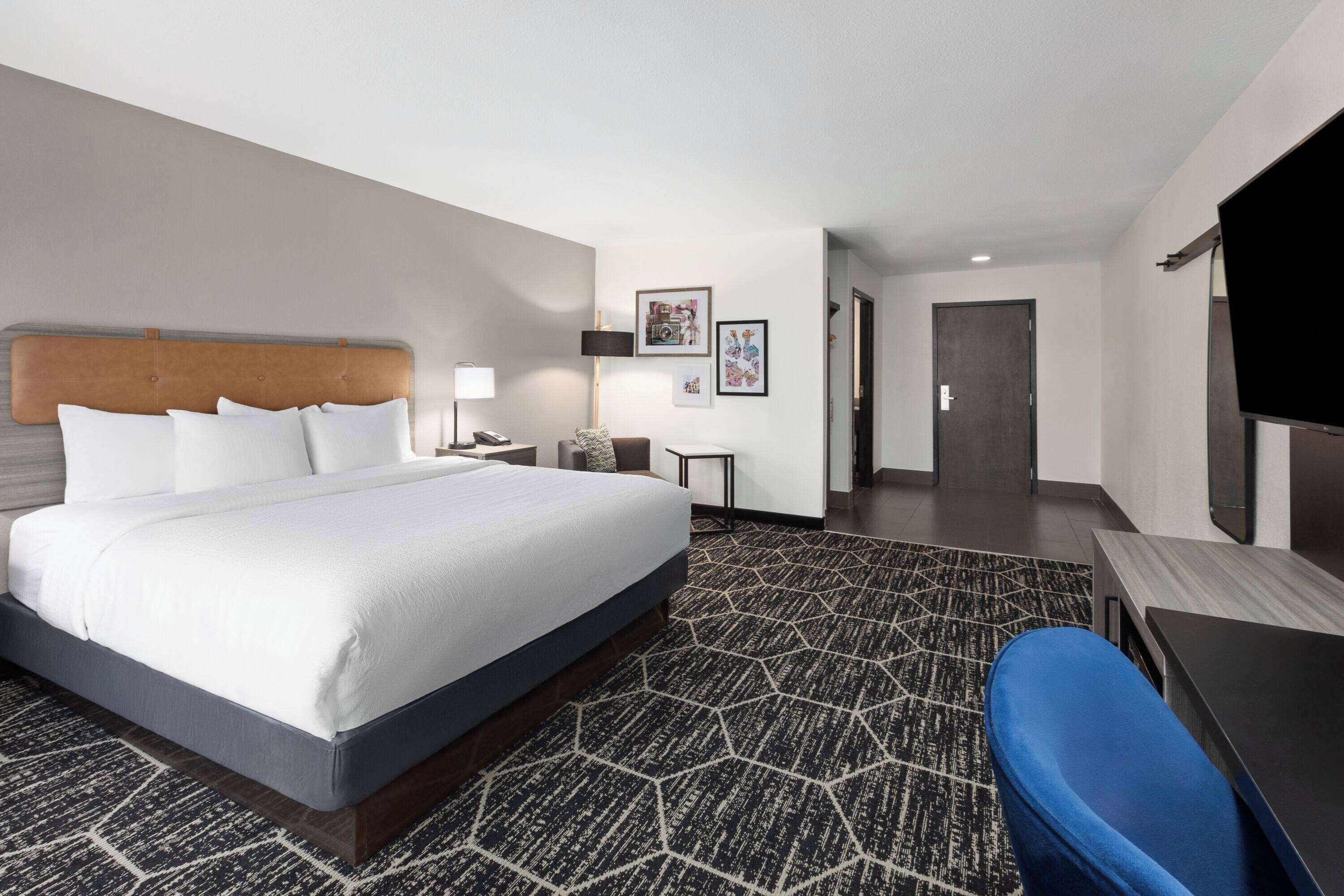 A hotel room with a large bed, a desk, a chair, a TV, and a door.