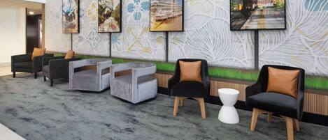 A lobby with a patterned wall, several chairs, and a small white table.