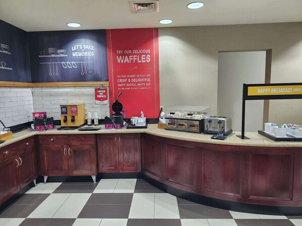 A kitchen area with a waffle station, a sign for breakfast, and a caution sign for hot surfaces. - Hampton Inn Great Falls (Great Falls)
