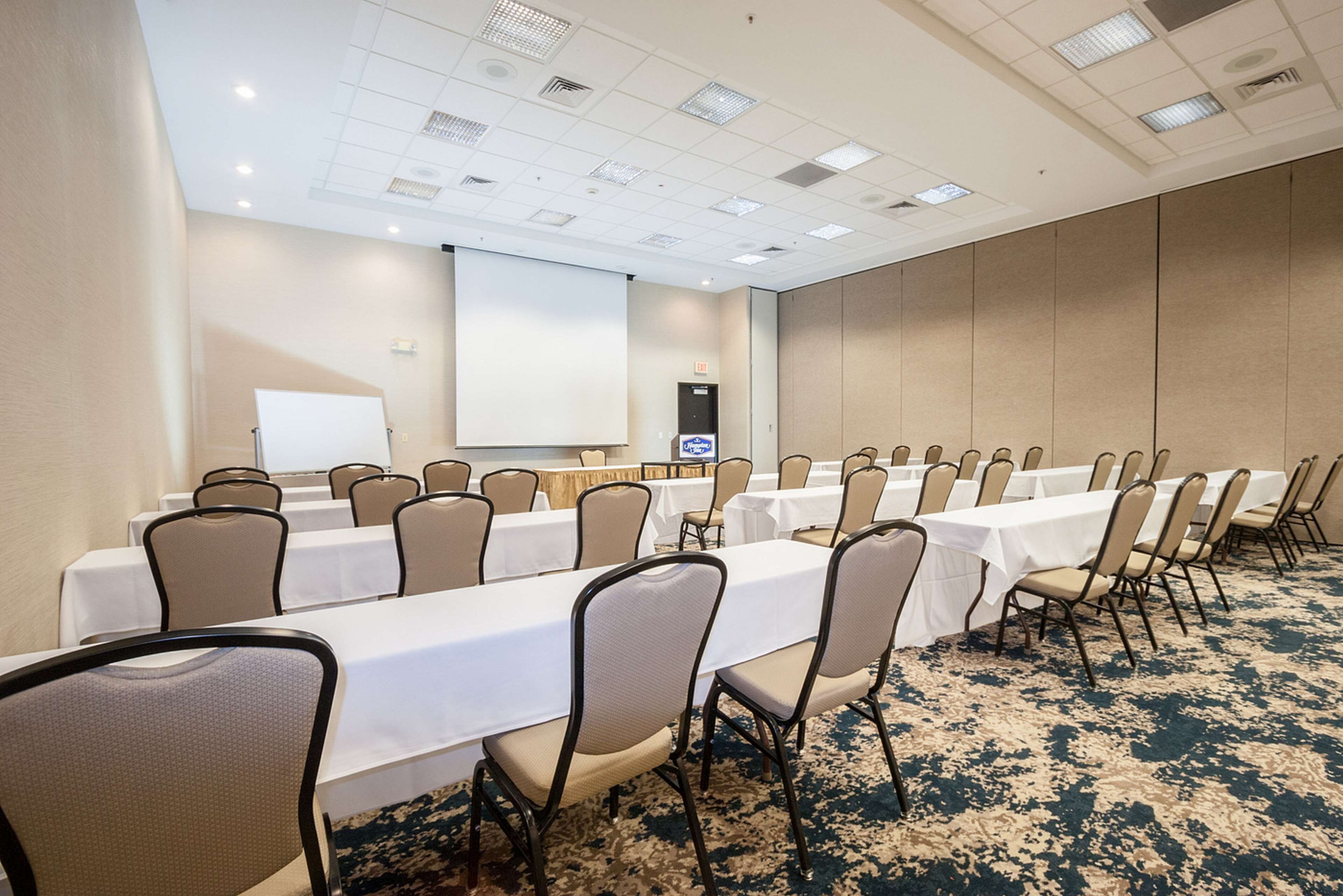 A conference room with multiple tables and chairs, a whiteboard, and a projector screen.