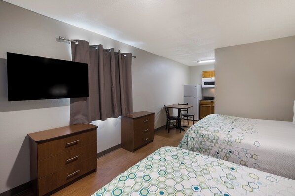 Habitación de hotel con dos camas, televisión, escritorio con silla y kitchenette.