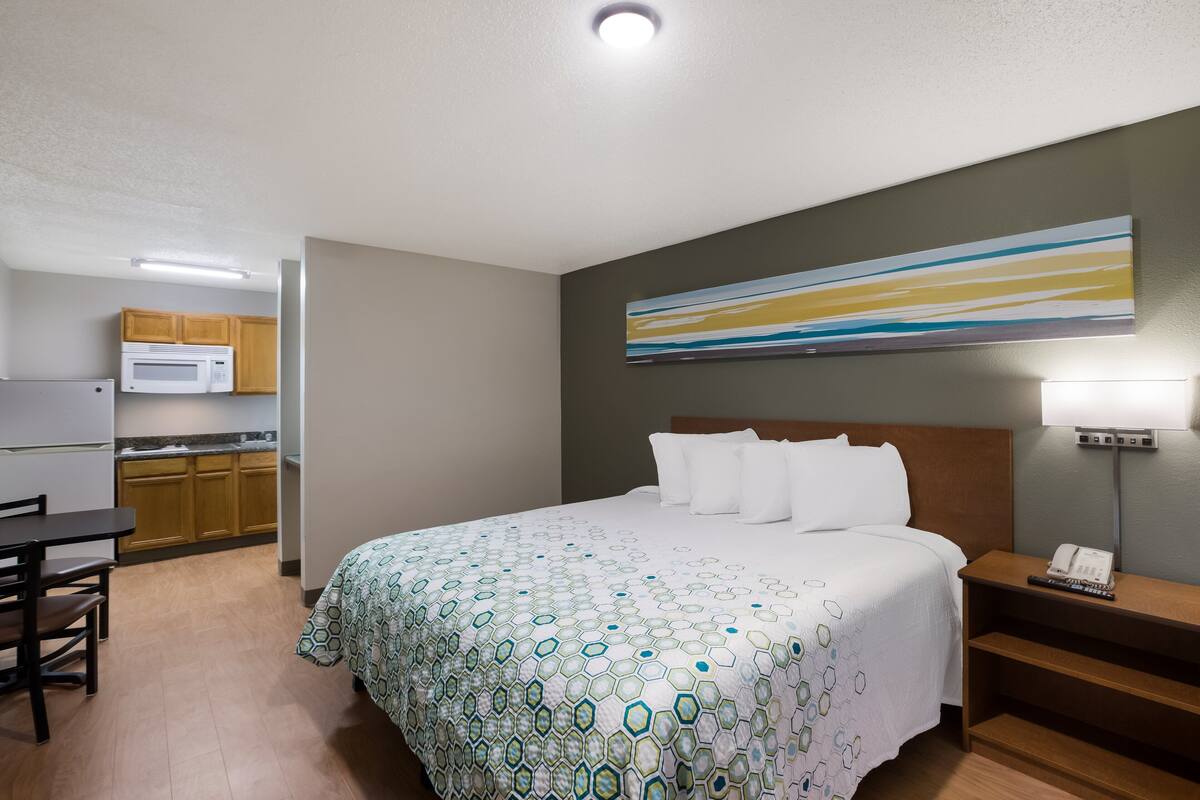 Una camera d'albergo con un letto, un comodino, una lampada e vista sull'area della cucina.