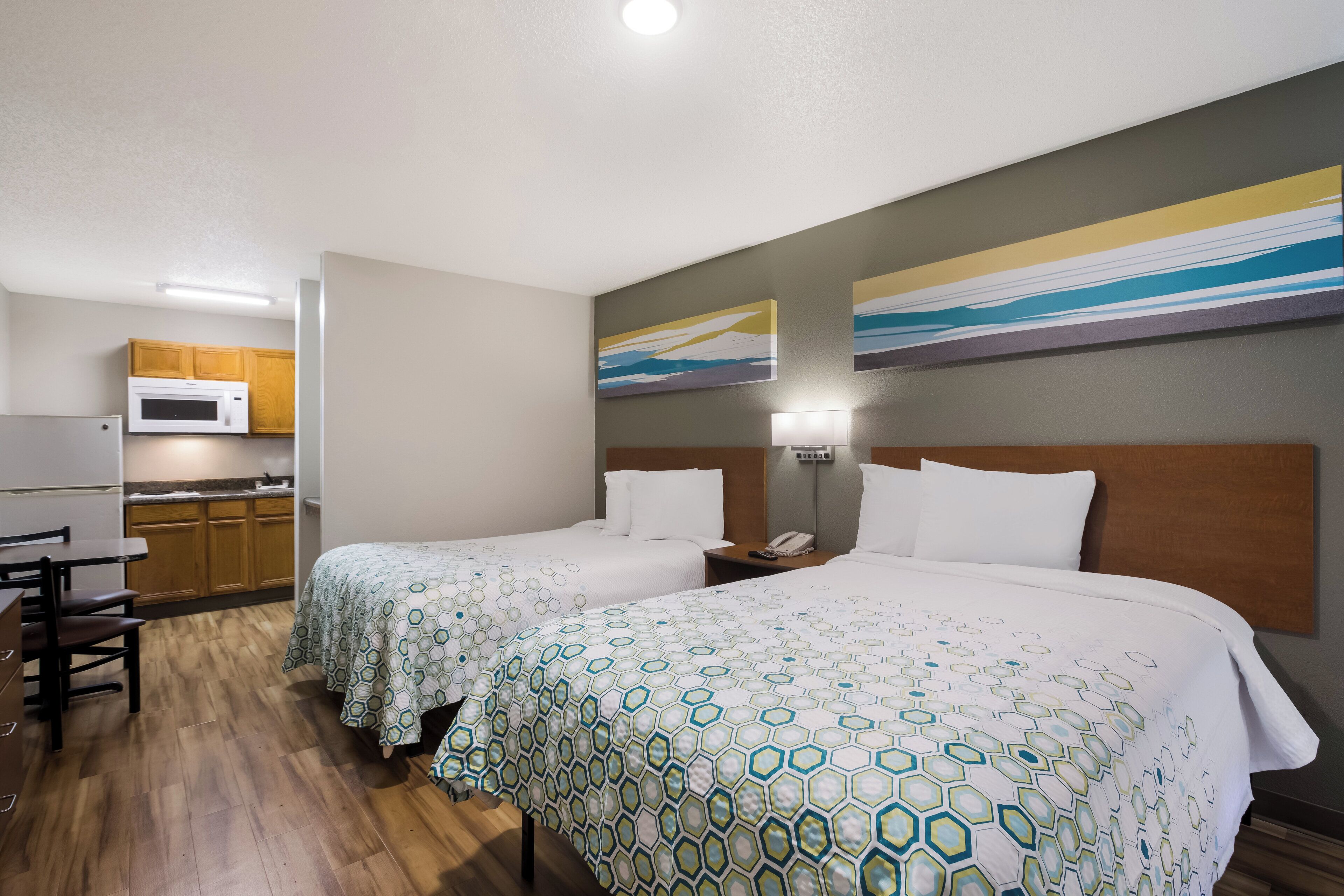 A hotel room with two beds, a kitchenette, and artwork on the walls.