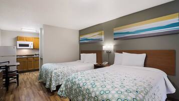 A hotel room with two beds, a kitchenette, and artwork on the walls.