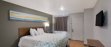A hotel room with a bed, a nightstand, a lamp, a television, and a door.