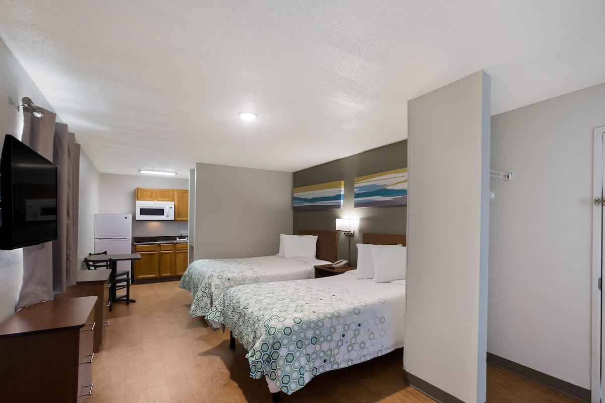 Ein Hotelzimmer mit zwei Betten, einer Küchenzeile, einem Fernseher und einem Bild an der Wand.