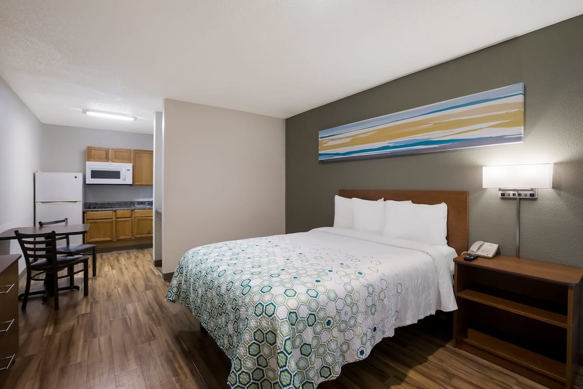 Ein Hotelzimmer mit einem Bett, einem Schreibtisch, einem Stuhl, einer Mikrowelle und einem Bild an der Wand.