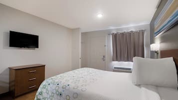 Habitación de hotel con una cama, cómoda, televisor en la pared y ventana con cortinas.