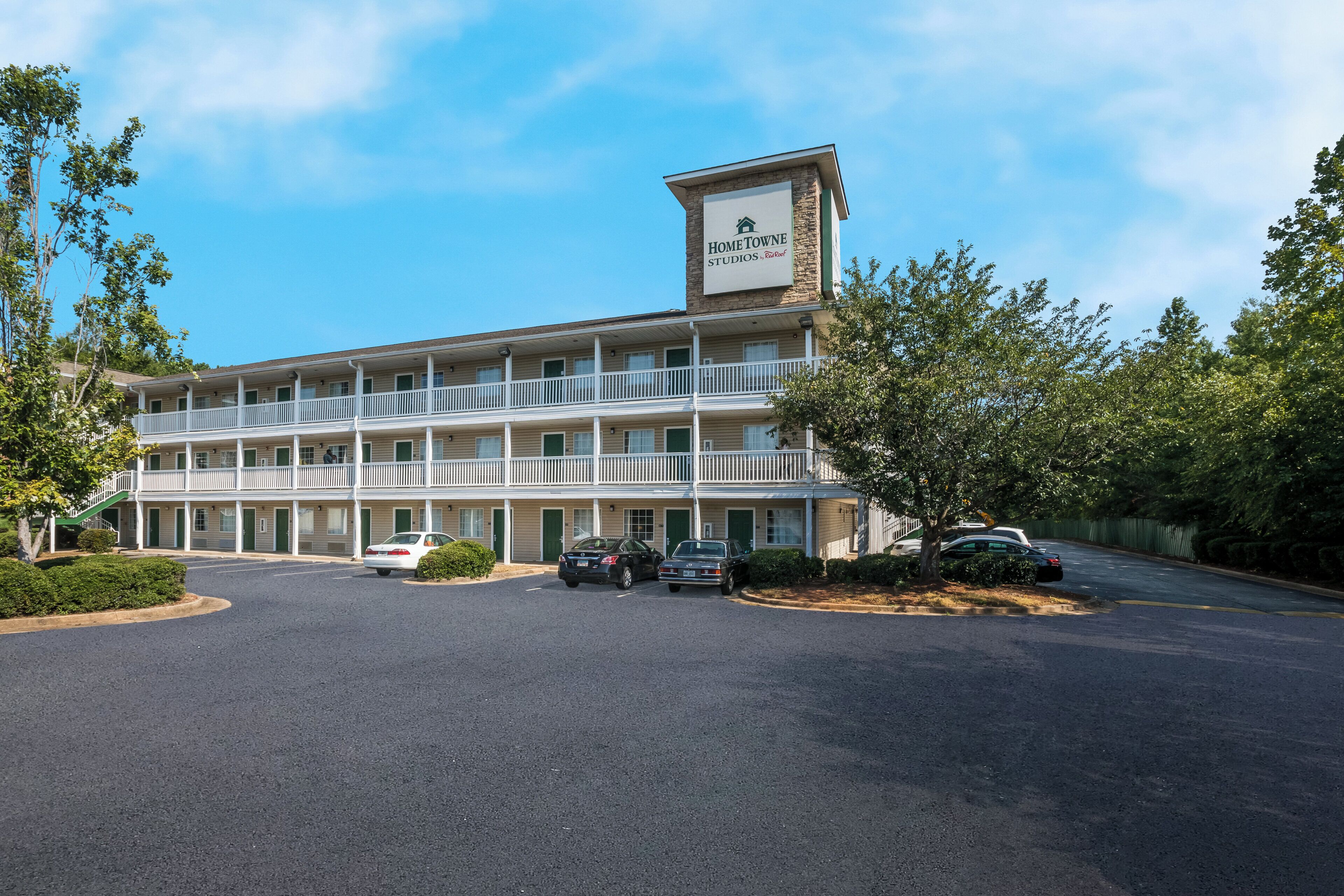 A multi-story motel with a central entrance, a parking lot, and a sign indicating 'Home Towne Studios RealRoof.'