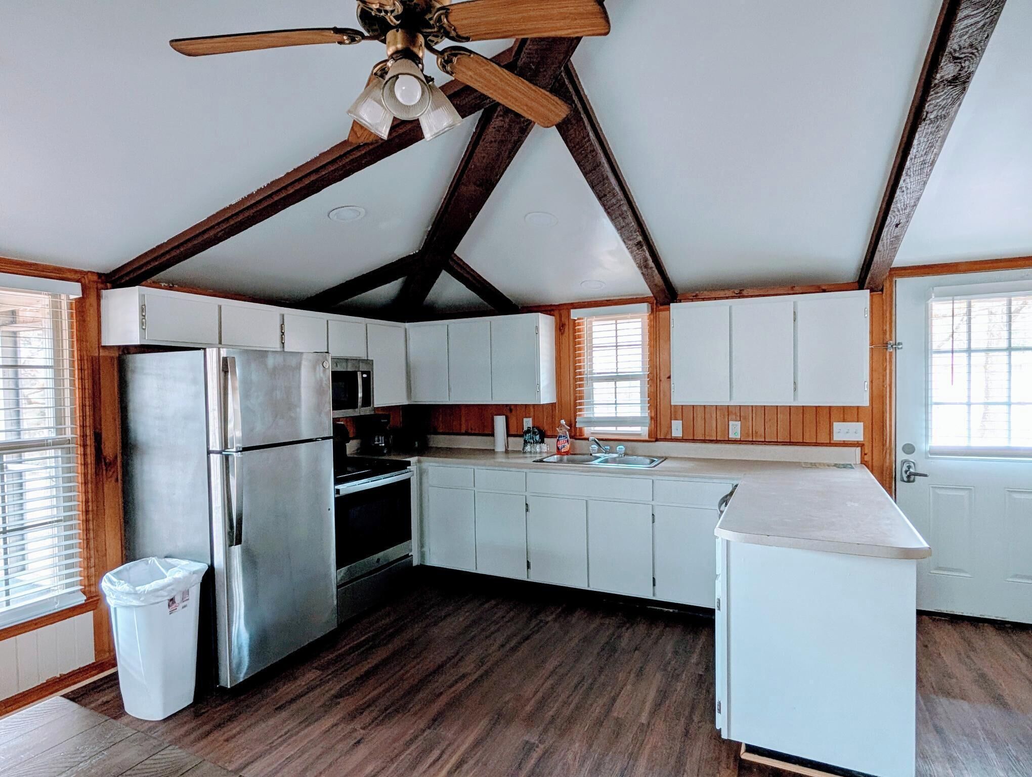 A kitchen with wooden beams, white cabinets, a stainless steel refrigerator, and a ceiling fan.