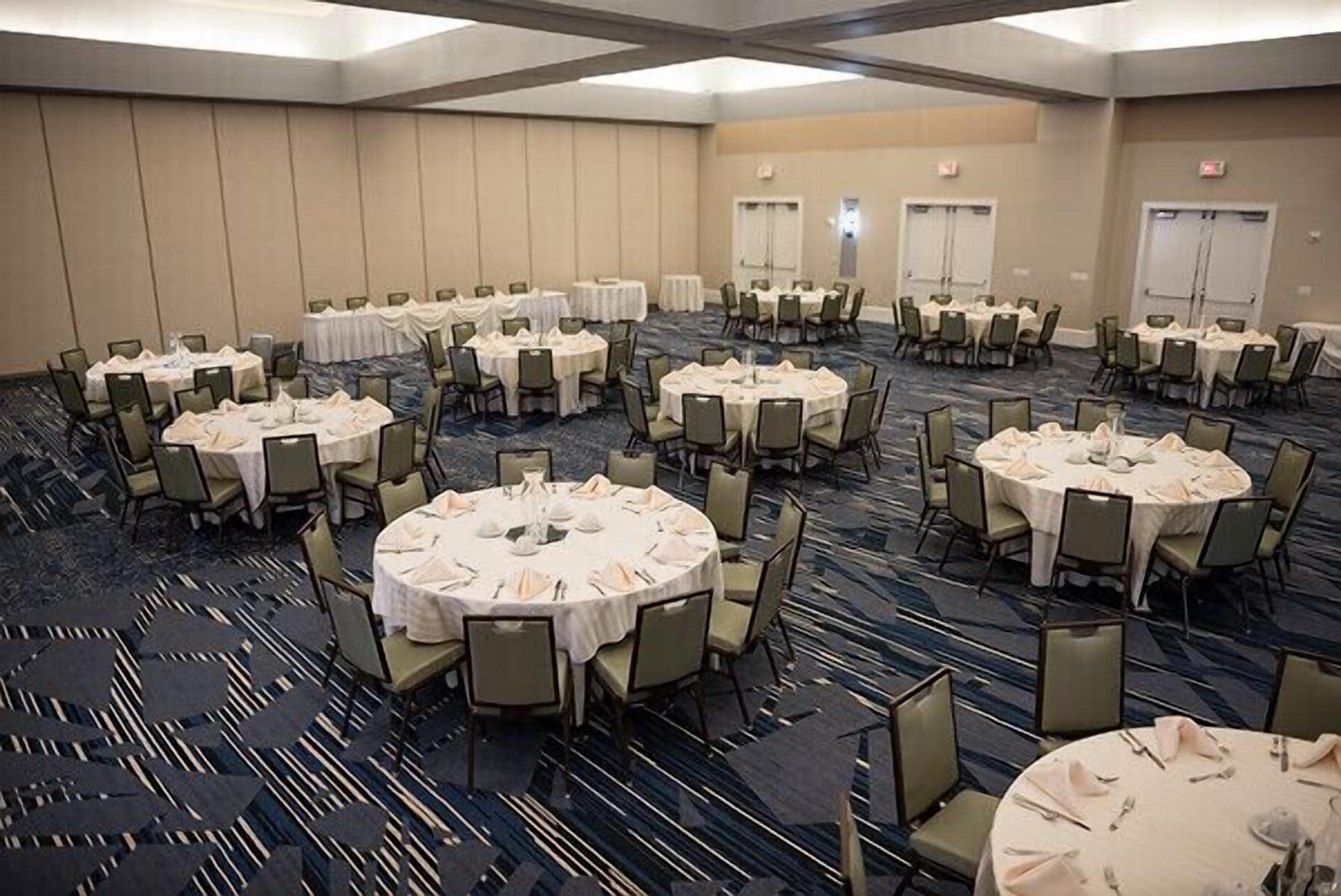 A large conference room with multiple round tables, each set with chairs and white tablecloths.