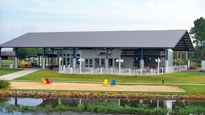 A building with a covered patio area, outdoor seating, and a pond in front. - Lake Blackshear Resort & Golf Club (Cordele)